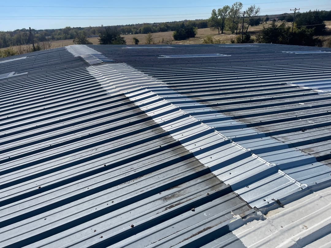 Metal roof with overlapping seams and a clear blue sky in the background.