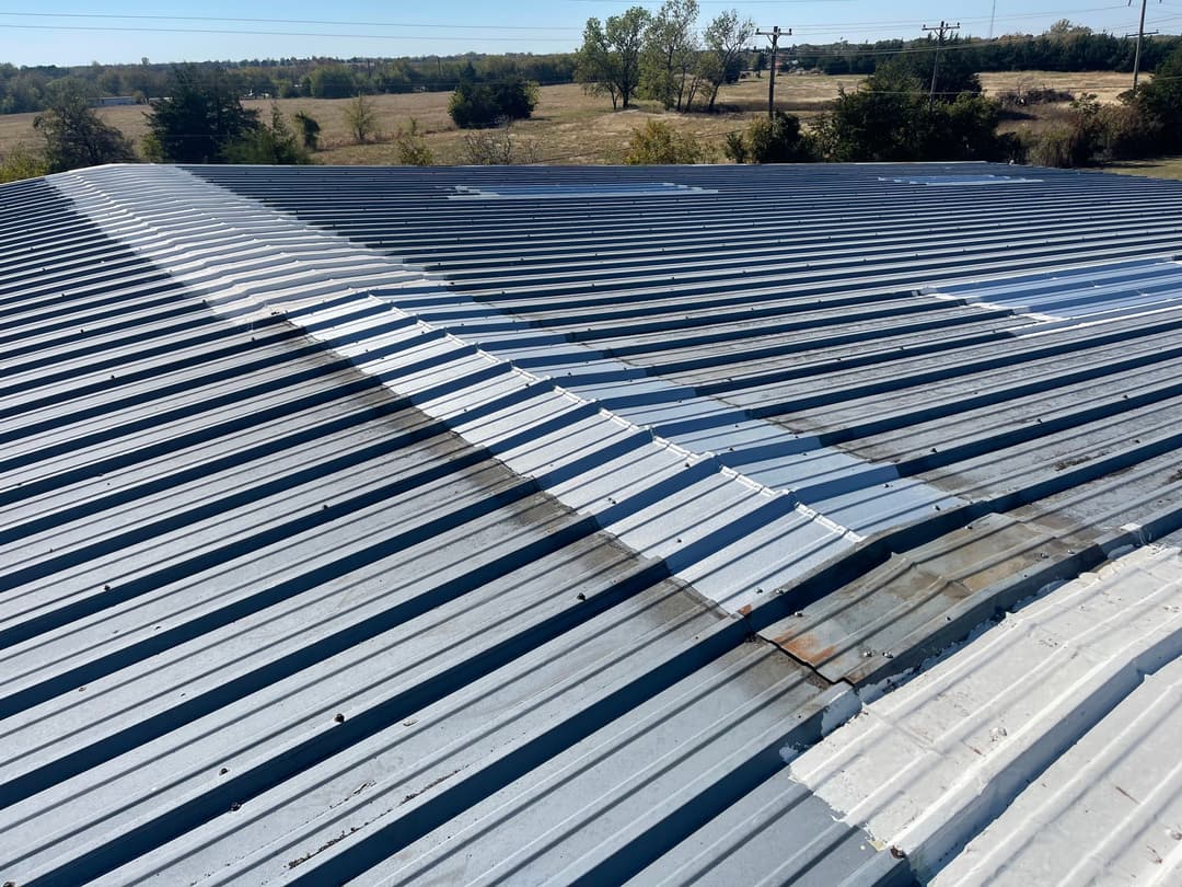 Metal roof with visible seams and weathered areas against a rural landscape.